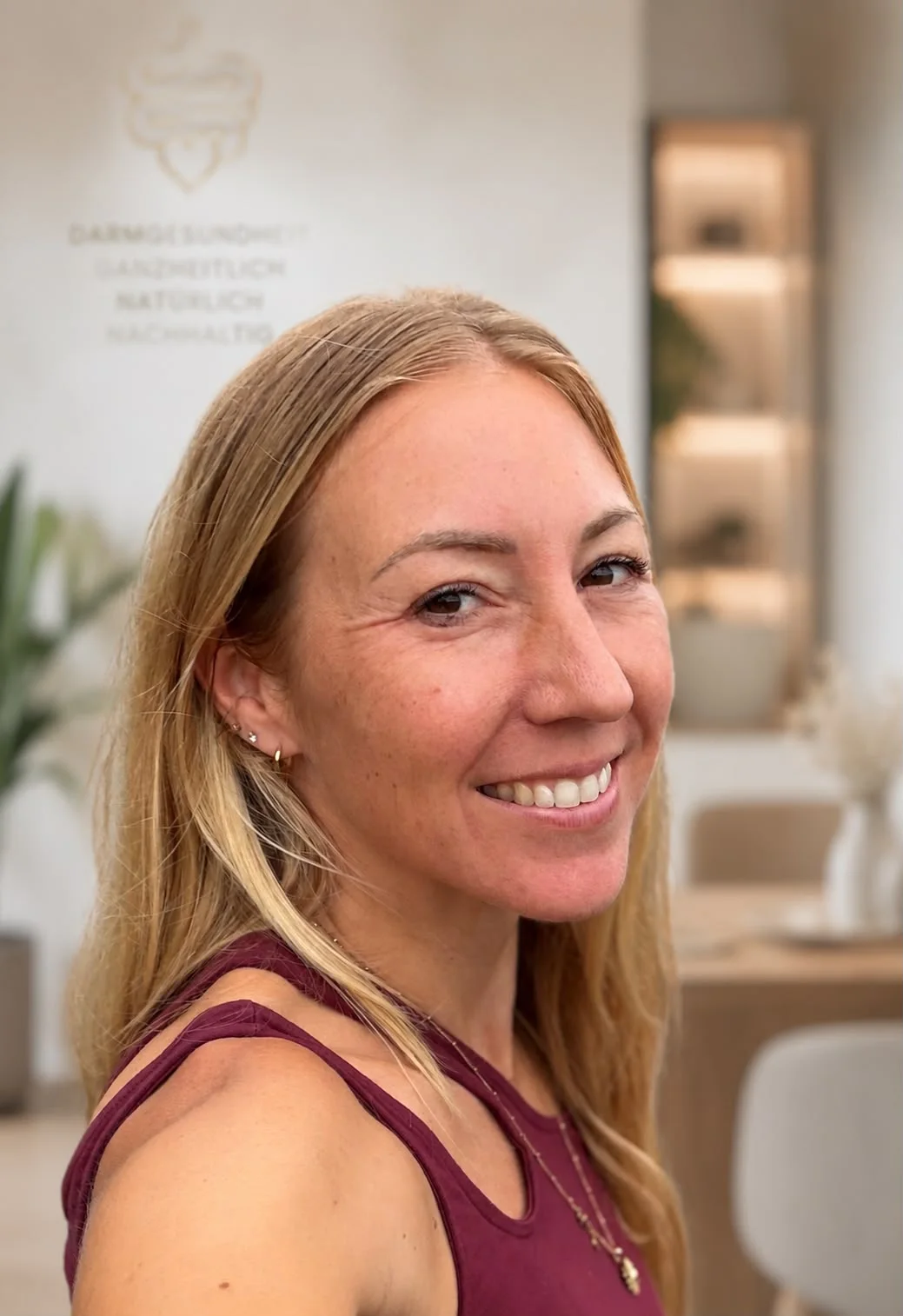 Christina, ganzheitliche Darmgesundheitsmentorin, lächelt in ihrem Studio vor der Wand mit dem MindBellySkin-Logo